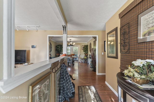 hallway featuring crown molding, rail lighting, a textured ceiling, dark hardwood / wood-style flooring, and a chandelier