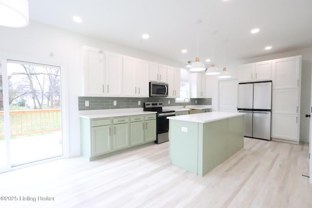 kitchen featuring appliances with stainless steel finishes, pendant lighting, white cabinetry, light hardwood / wood-style flooring, and a kitchen island