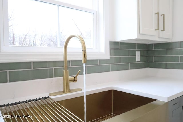 interior details featuring white cabinets, decorative backsplash, and sink