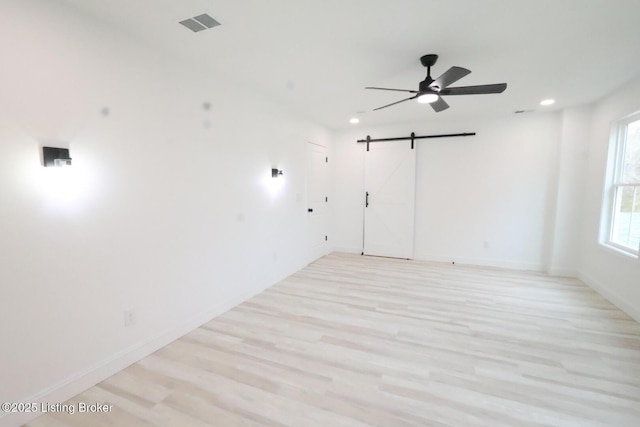 empty room with a barn door, light hardwood / wood-style floors, and ceiling fan