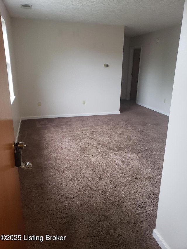 spare room featuring dark carpet and a textured ceiling