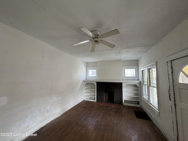 unfurnished living room with ceiling fan, dark hardwood / wood-style floors, a textured ceiling, and a brick fireplace