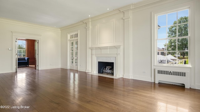 unfurnished living room with radiator, a premium fireplace, a healthy amount of sunlight, and ornamental molding