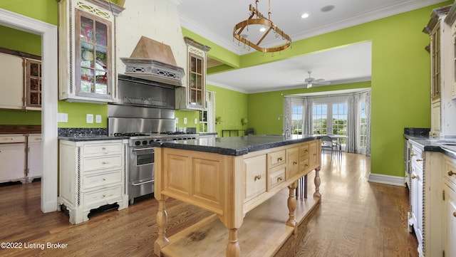 kitchen with ornamental molding, custom range hood, high end stainless steel range oven, ceiling fan, and wood-type flooring