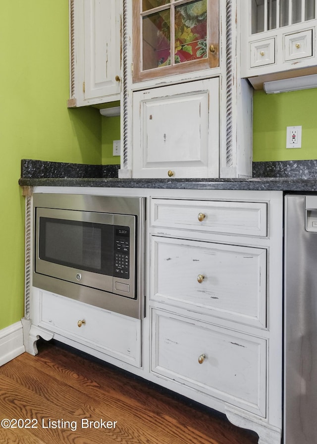 kitchen featuring dark hardwood / wood-style flooring, stainless steel appliances, white cabinetry, and dark stone countertops