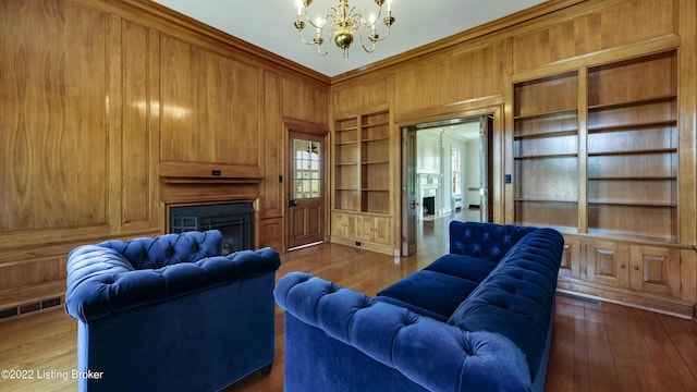 living room featuring a chandelier, built in shelves, dark hardwood / wood-style flooring, and wooden walls