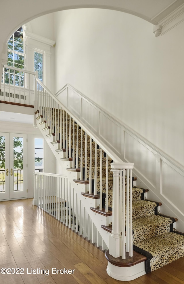 stairs featuring french doors, a towering ceiling, and wood-type flooring