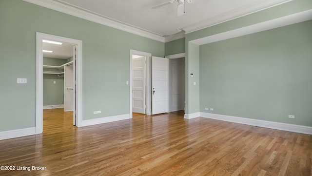 unfurnished bedroom featuring a walk in closet, ceiling fan, crown molding, light hardwood / wood-style flooring, and a closet