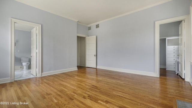 unfurnished bedroom featuring crown molding, hardwood / wood-style flooring, a spacious closet, connected bathroom, and a closet