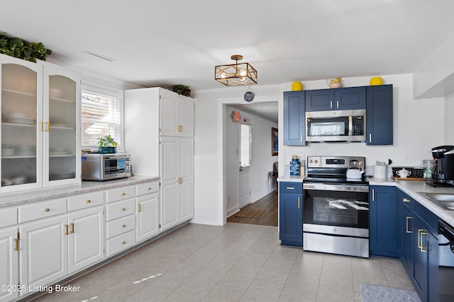 kitchen with light tile patterned floors, blue cabinets, appliances with stainless steel finishes, white cabinets, and ornamental molding