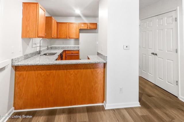 kitchen featuring kitchen peninsula, dark hardwood / wood-style flooring, light stone countertops, and sink