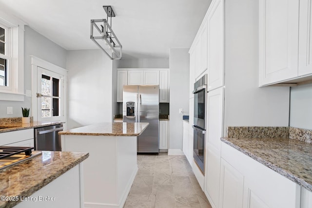 kitchen featuring appliances with stainless steel finishes, hanging light fixtures, light stone countertops, white cabinets, and a kitchen island