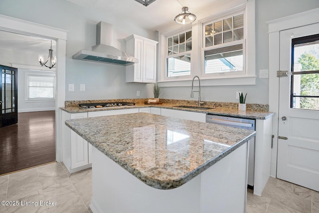 kitchen with appliances with stainless steel finishes, sink, wall chimney range hood, and white cabinets