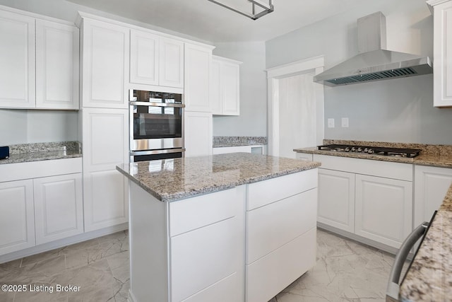 kitchen with appliances with stainless steel finishes, wall chimney exhaust hood, light stone countertops, and white cabinets