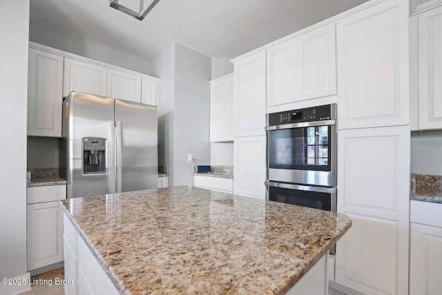 kitchen featuring light stone countertops, white cabinetry, appliances with stainless steel finishes, and a center island