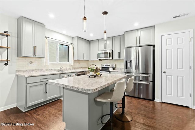 kitchen with dark hardwood / wood-style flooring, gray cabinetry, stainless steel appliances, decorative light fixtures, and a kitchen island