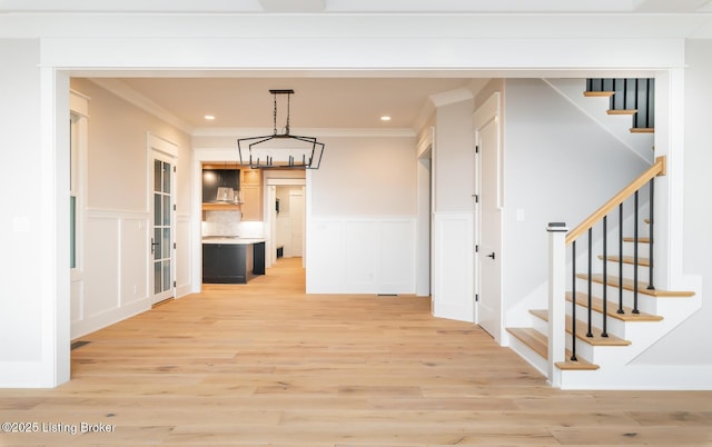 hall with crown molding, light hardwood / wood-style floors, and an inviting chandelier