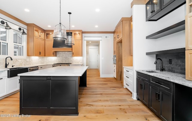 kitchen featuring decorative light fixtures, a kitchen island, sink, and light hardwood / wood-style flooring