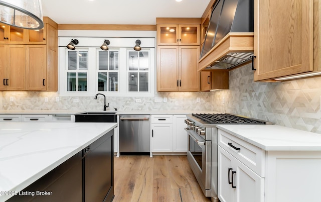 kitchen with premium range hood, light stone counters, stainless steel appliances, light hardwood / wood-style floors, and white cabinetry