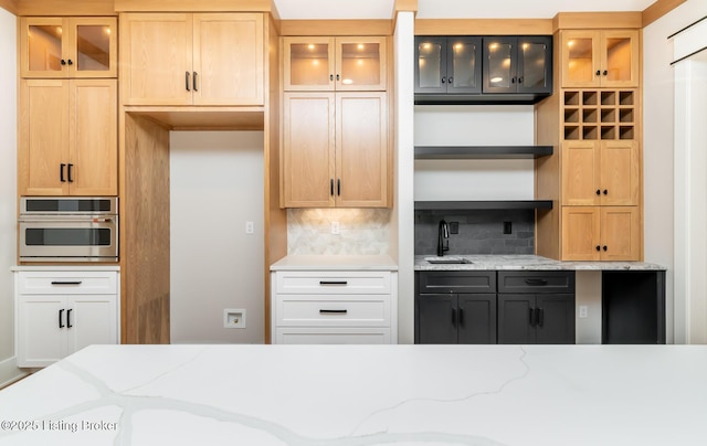 kitchen with light stone countertops, sink, white cabinetry, tasteful backsplash, and oven