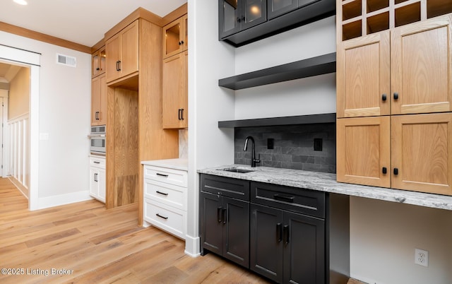 kitchen featuring decorative backsplash, light wood-type flooring, light stone counters, stainless steel oven, and sink