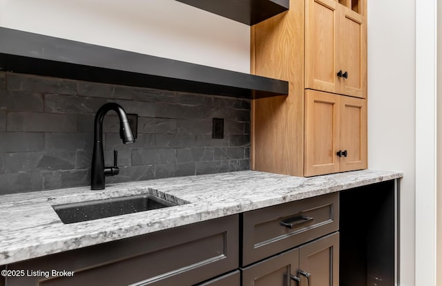 kitchen with backsplash, light stone counters, and sink