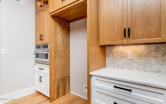 kitchen with wall oven, light stone counters, light hardwood / wood-style floors, decorative backsplash, and white cabinets