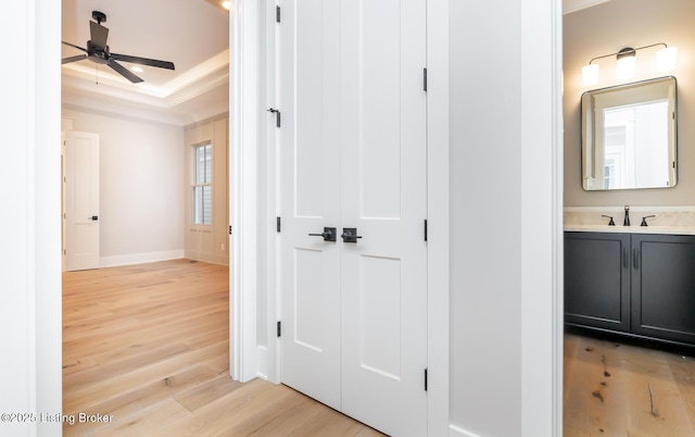 corridor featuring a raised ceiling, sink, and light wood-type flooring