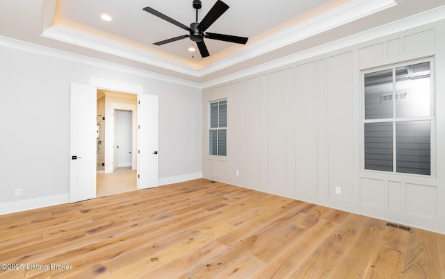 spare room featuring a raised ceiling, crown molding, and light hardwood / wood-style floors