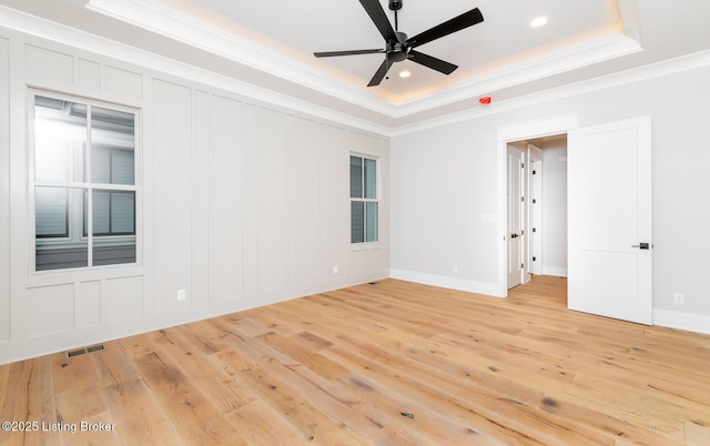 empty room featuring ceiling fan, ornamental molding, light hardwood / wood-style flooring, and a tray ceiling