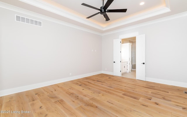 empty room with a raised ceiling, crown molding, ceiling fan, and light hardwood / wood-style floors