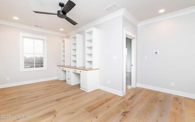 interior space featuring light wood-type flooring, built in shelves, ceiling fan, crown molding, and built in desk