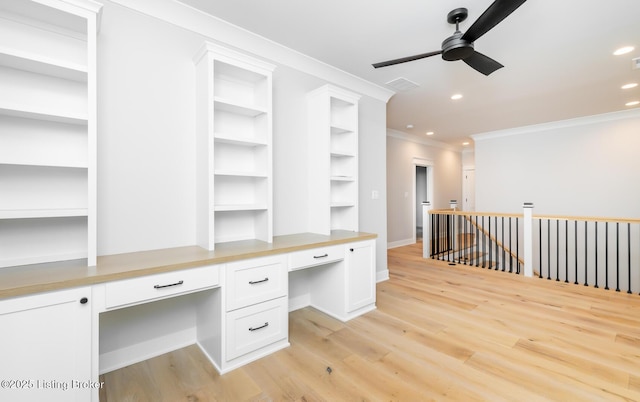 unfurnished office with light wood-type flooring, built in desk, ceiling fan, and ornamental molding