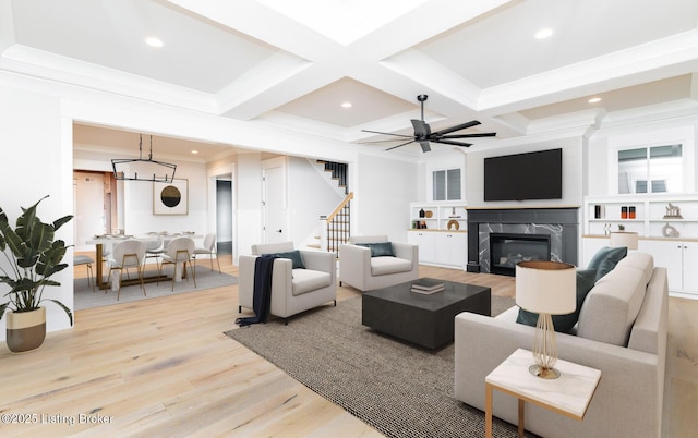 living room with ceiling fan, built in shelves, light wood-type flooring, a fireplace, and beam ceiling