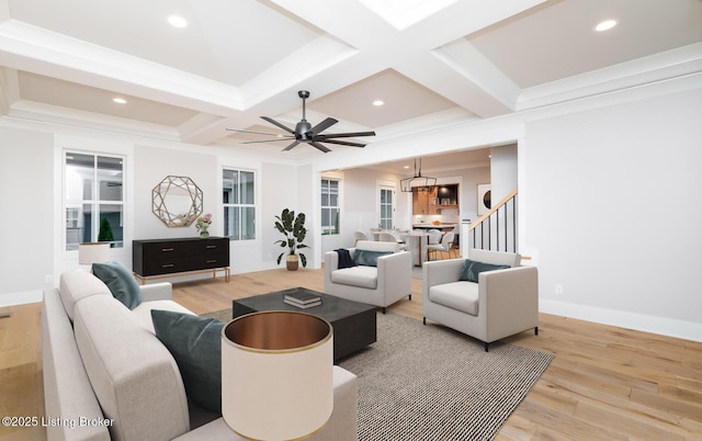 living room with ceiling fan with notable chandelier, beam ceiling, light wood-type flooring, and coffered ceiling