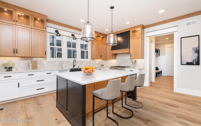 kitchen featuring white cabinetry, a center island, hanging light fixtures, light hardwood / wood-style floors, and custom exhaust hood