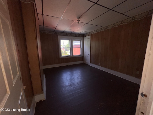 spare room featuring dark hardwood / wood-style floors, a paneled ceiling, and wooden walls