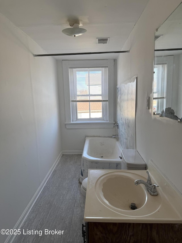 bathroom with hardwood / wood-style flooring, a tub to relax in, vanity, and toilet