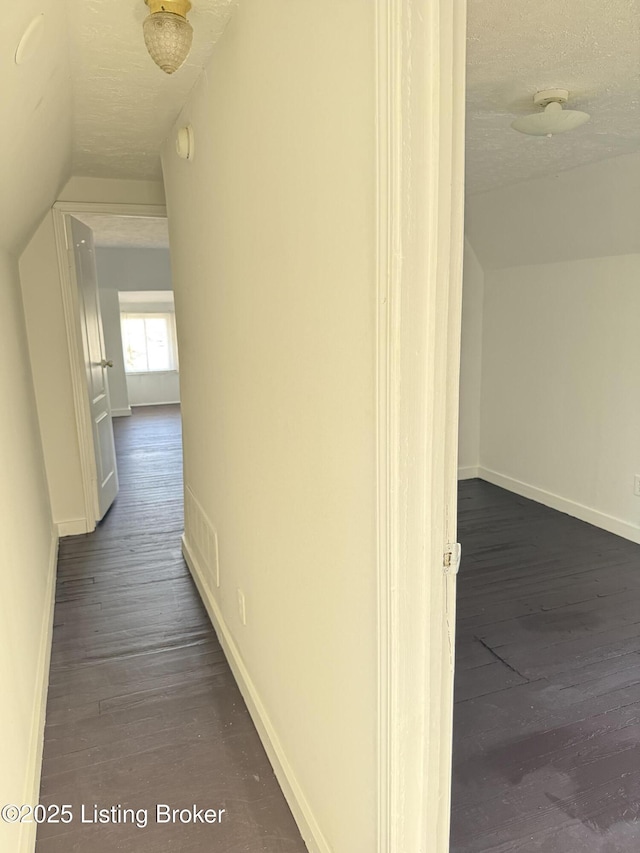 corridor featuring dark hardwood / wood-style flooring, vaulted ceiling, and a textured ceiling