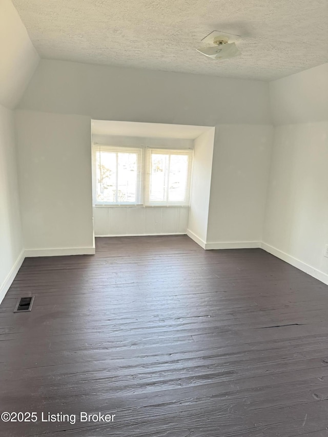 additional living space with lofted ceiling, dark hardwood / wood-style floors, and a textured ceiling