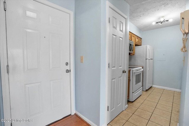 kitchen featuring a textured ceiling, light tile patterned floors, and white appliances