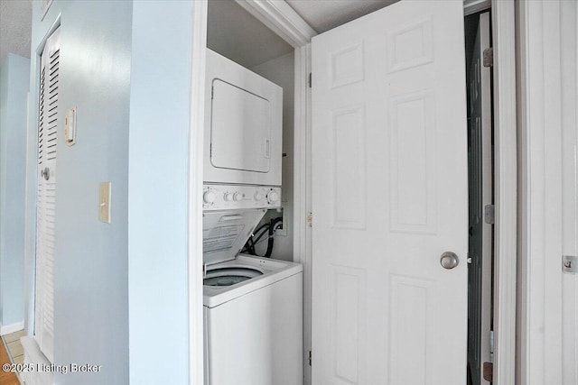 laundry area with a textured ceiling and stacked washer / drying machine