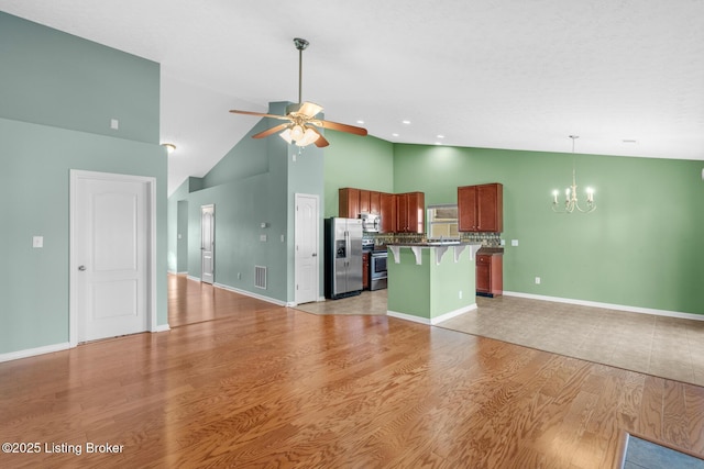 kitchen with a kitchen bar, stainless steel appliances, high vaulted ceiling, a kitchen island, and light hardwood / wood-style flooring