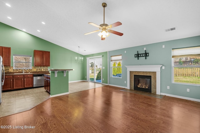 unfurnished living room with ceiling fan with notable chandelier, lofted ceiling, a fireplace, sink, and hardwood / wood-style flooring