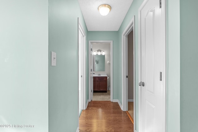 hall with a textured ceiling, hardwood / wood-style floors, and sink