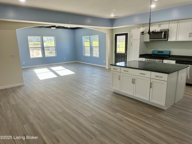 kitchen with white cabinets, stainless steel appliances, decorative light fixtures, and light hardwood / wood-style floors