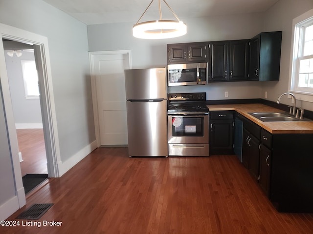 kitchen featuring sink, wooden counters, dark hardwood / wood-style floors, pendant lighting, and appliances with stainless steel finishes