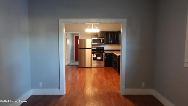 kitchen with dark brown cabinetry, pendant lighting, stainless steel appliances, and wood-type flooring