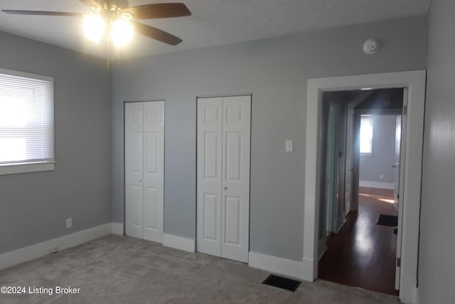 unfurnished bedroom with carpet floors, two closets, and ceiling fan