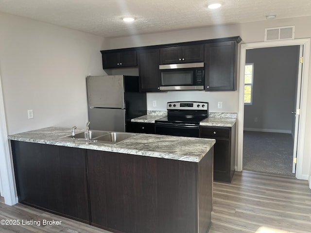 kitchen featuring kitchen peninsula, a textured ceiling, stainless steel appliances, sink, and light hardwood / wood-style flooring